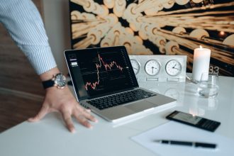 Mesa de trabalho com laptop exibindo gráfico financeiro e outros dispositivos tecnológicos.