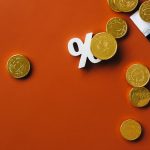 Moedas douradas sobre um gráfico do mercado financeiro, acompanhadas de um símbolo de porcentagem.