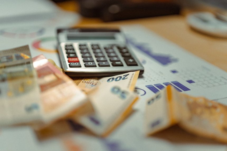 Cédulas de euro e calculadora sobre documentos financeiros, em uma composição que remete a orçamento e contabilidade.