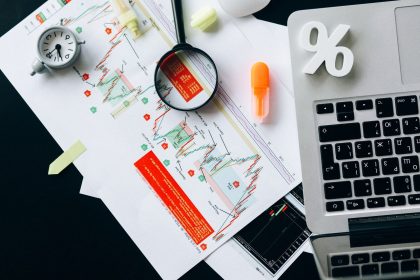 Documentos financeiros com gráficos e um laptop organizados sobre uma mesa de trabalho.