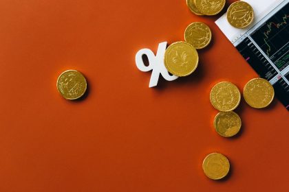 Moedas douradas sobre um gráfico do mercado financeiro, acompanhadas de um símbolo de porcentagem.